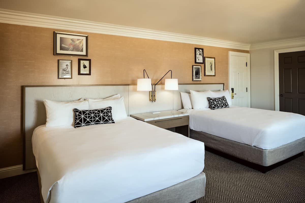 A hotel room with two beds, a nightstand with a lamp, and framed pictures on the wall.