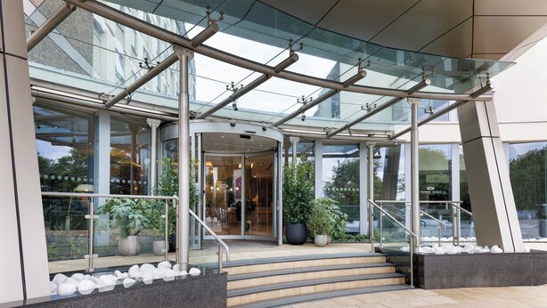Entrada de un edificio moderno con puertas de vidrio, una escalera y plantas en macetas.
