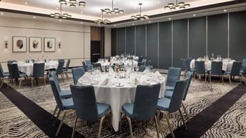 A conference room with round tables, blue chairs, and white tablecloths, featuring modern lighting and a patterned carpet.
