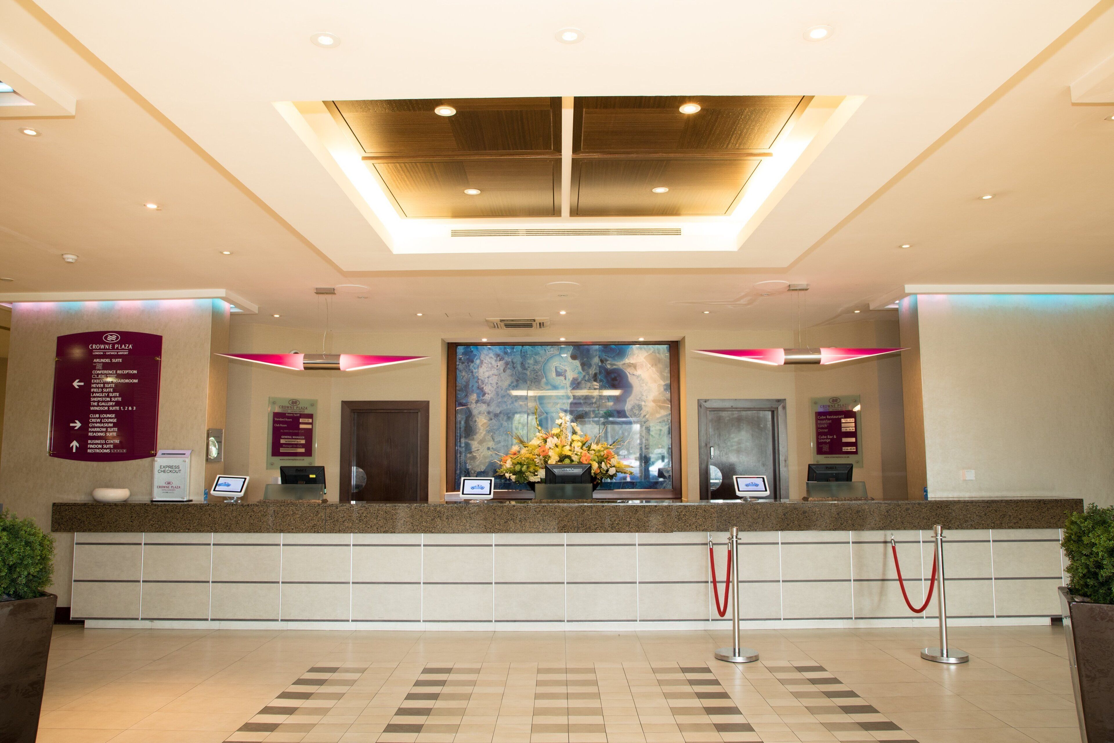A hotel reception area with a marble counter, a large floral arrangement, and directional signs.