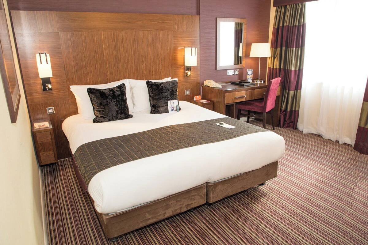 A hotel room with a large bed, a desk, a chair, and a mirror.