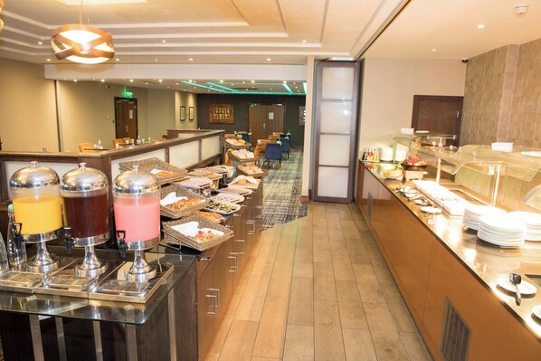 A buffet area with various food items and beverages, a reception desk, and seating area in the background. - Crowne Plaza London- Gatwick Airport by IHG (Crawley)