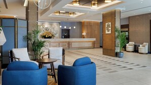 Un vestíbulo moderno con mostrador de recepción, zona de estar con sillas azules y plantas decorativas.