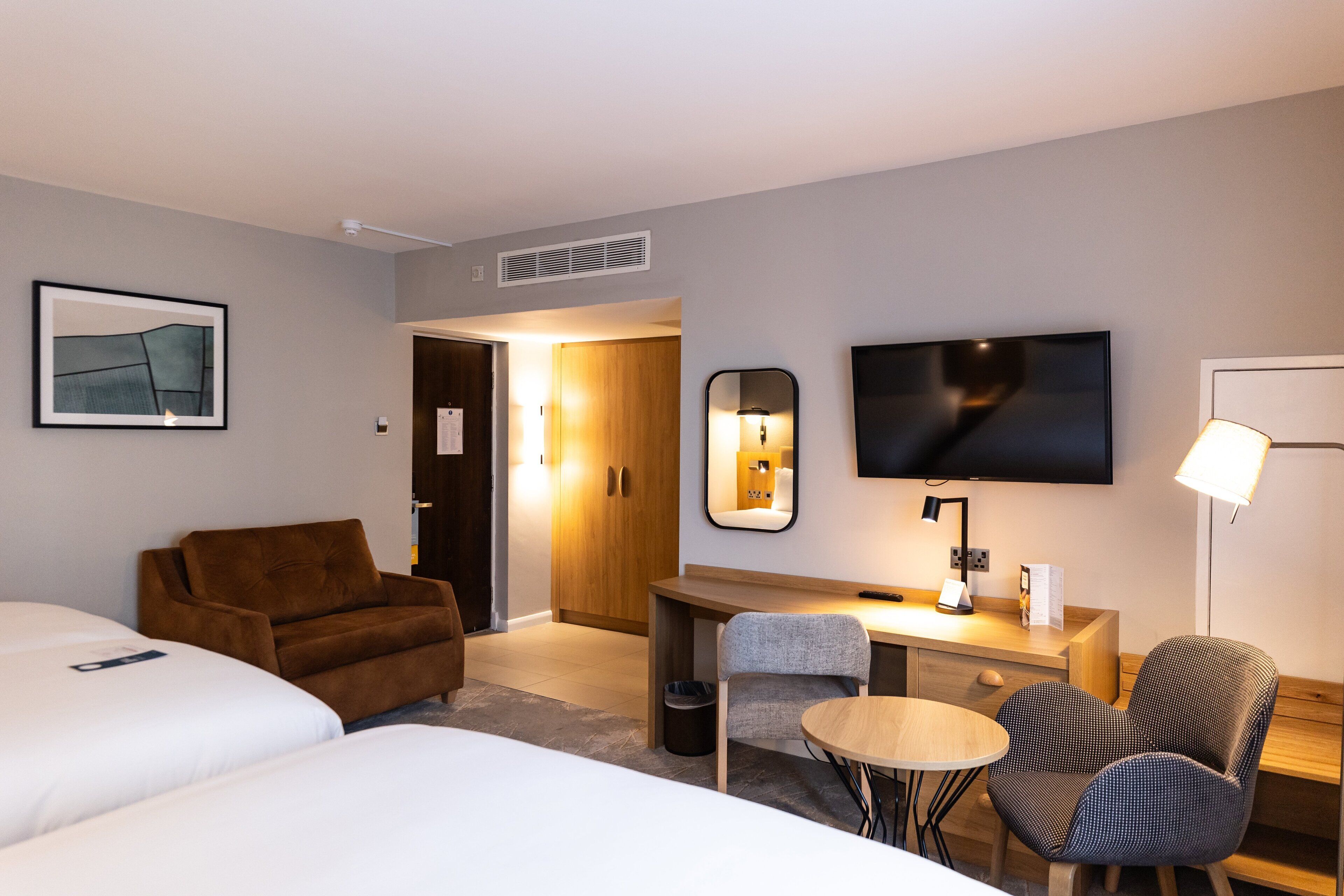 A hotel room with two beds, a desk, a chair, a TV, and a mirror.