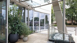 Una entrada moderna a un edificio con puertas de vidrio, plantas en macetas y una escalera de metal.