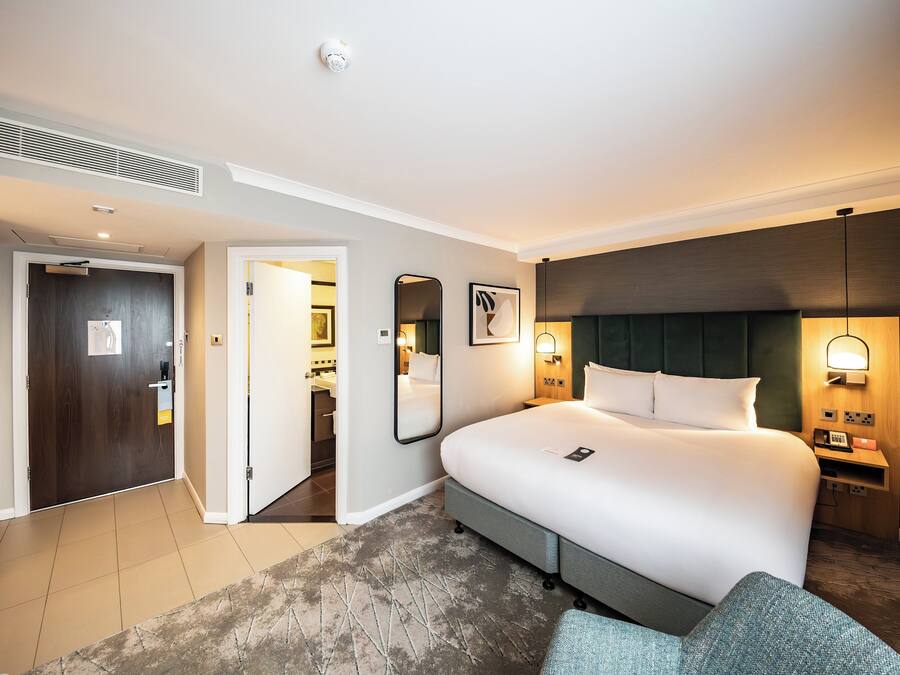 A hotel room with a large bed, bedside tables, a wardrobe, and a bathroom visible through an open door.