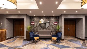 A lobby with a reception desk, two sofas, two armchairs, a patterned wall, and a ceiling with recessed lighting.