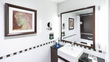 A modern bathroom with a large mirror, a framed artwork, a sink, and toiletries.