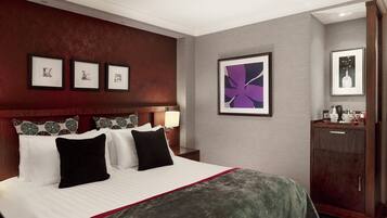 A hotel room with a large bed, a nightstand with a lamp, a dresser, and framed artwork on the walls.