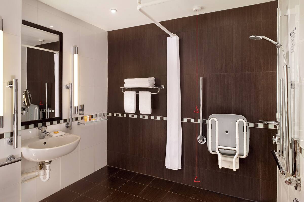 A modern bathroom with a white sink, a mirror, a shower with a handheld showerhead, and a towel rack.