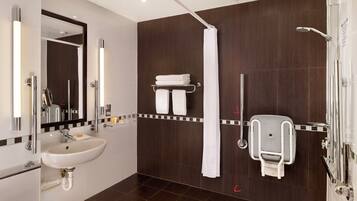 A modern bathroom with a white sink, a mirror, a shower with a handheld showerhead, and a towel rack.