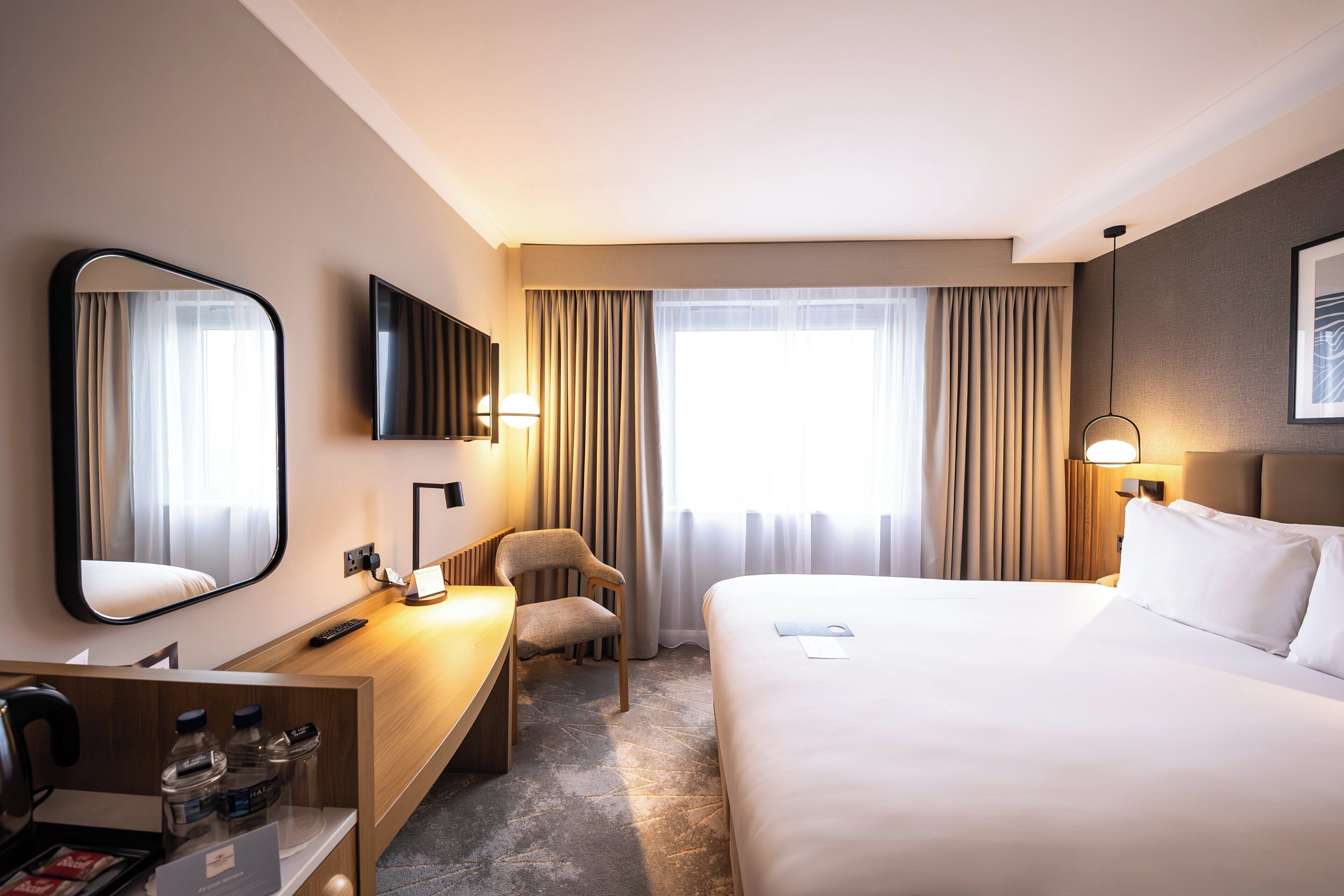 Habitación de hotel con cama, escritorio con silla, televisor y ventana con cortinas.