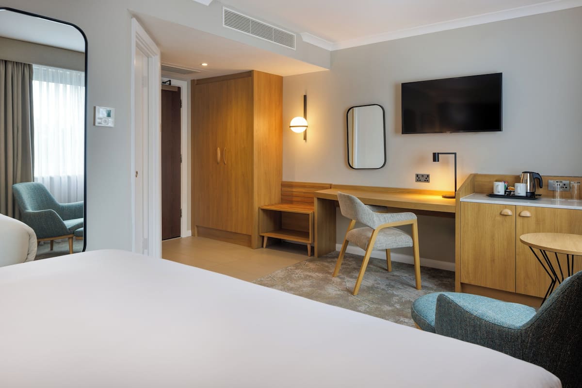 A hotel room with a bed, a desk with a chair, a TV, and a wardrobe.
