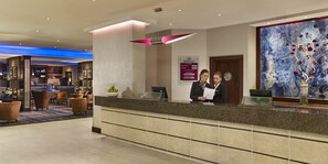 A hotel reception area with a counter, seating area, and a large abstract painting. - Crowne Plaza London- Gatwick Airport by IHG (Crawley)