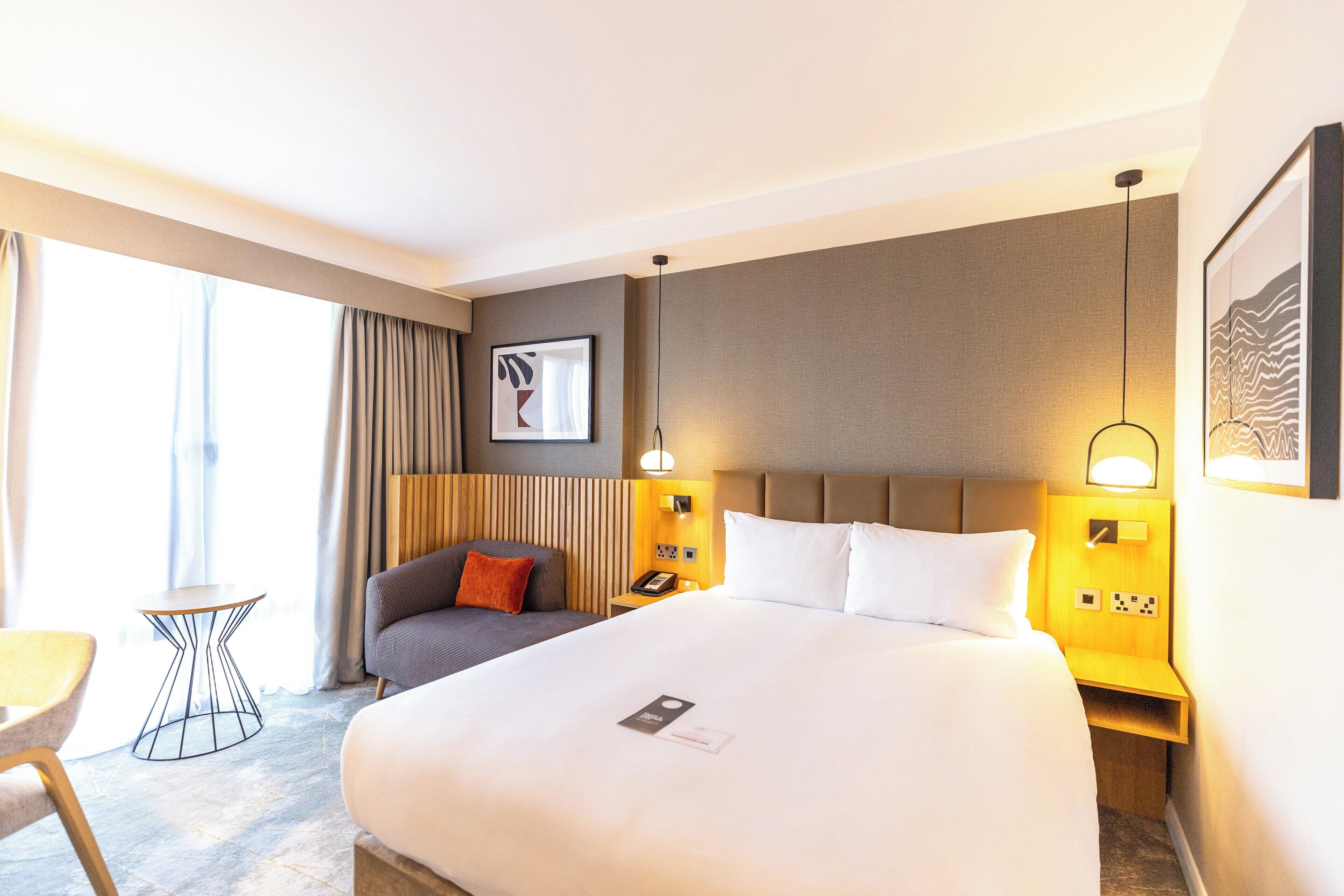 A hotel room with a large bed, bedside tables, a small table, and a chair.