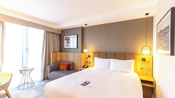A hotel room with a large bed, bedside tables, a small table, and a chair.