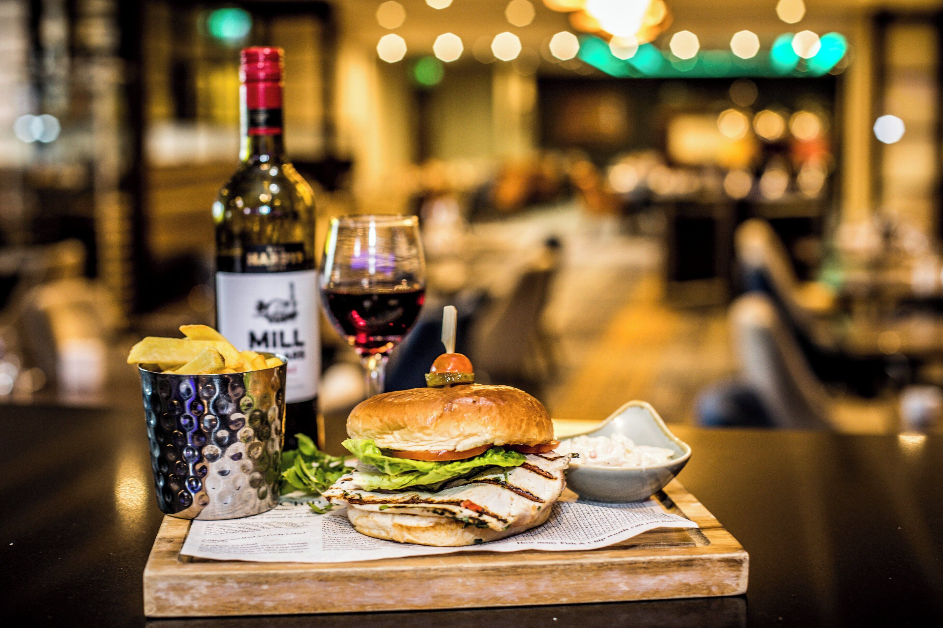Un repas composé d’un hamburger, de frites et d’une boisson, le tout servi sur une planche en bois.