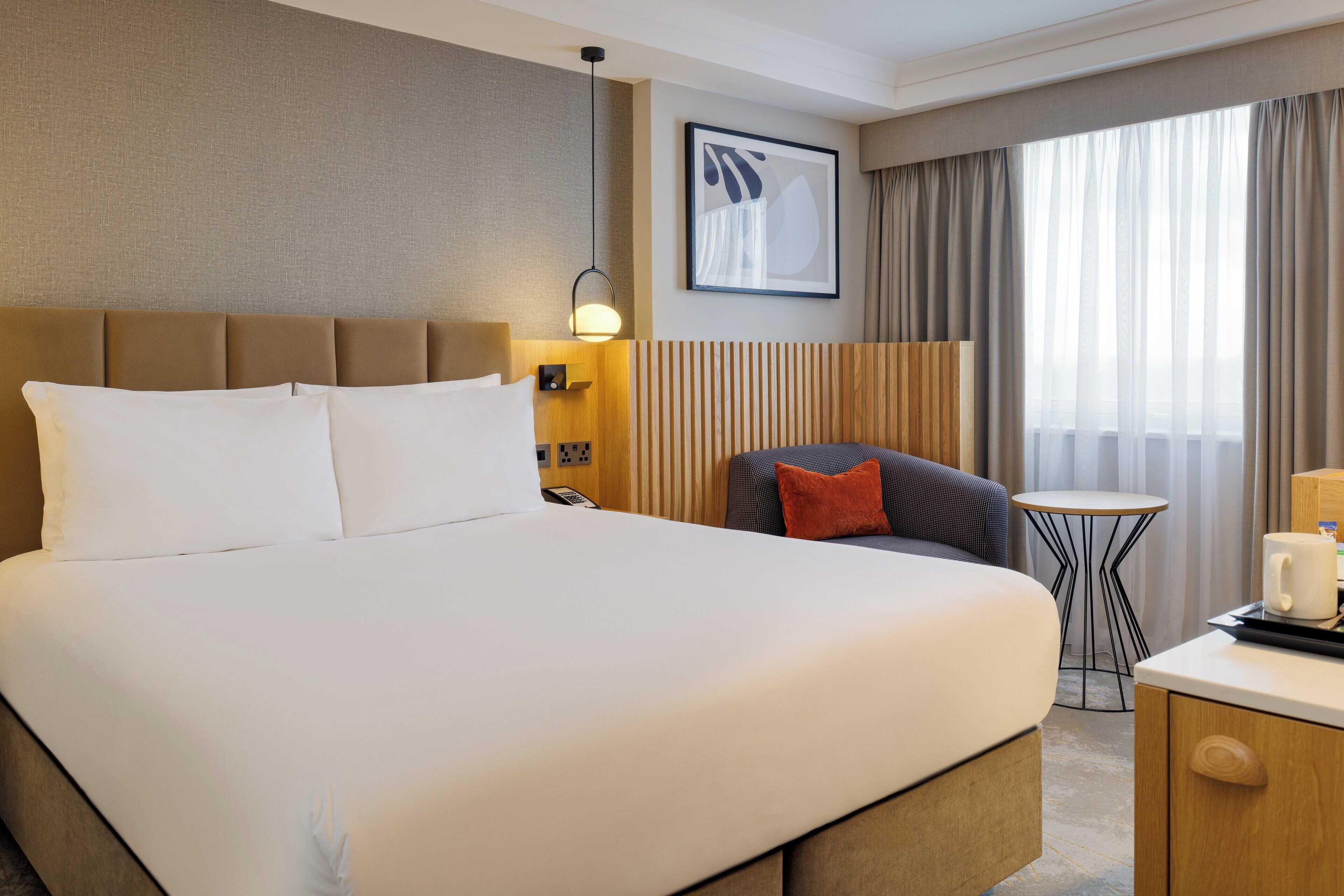 Une chambre d’hôtel avec un grand lit, une petite table, une chaise et une fenêtre avec des rideaux.