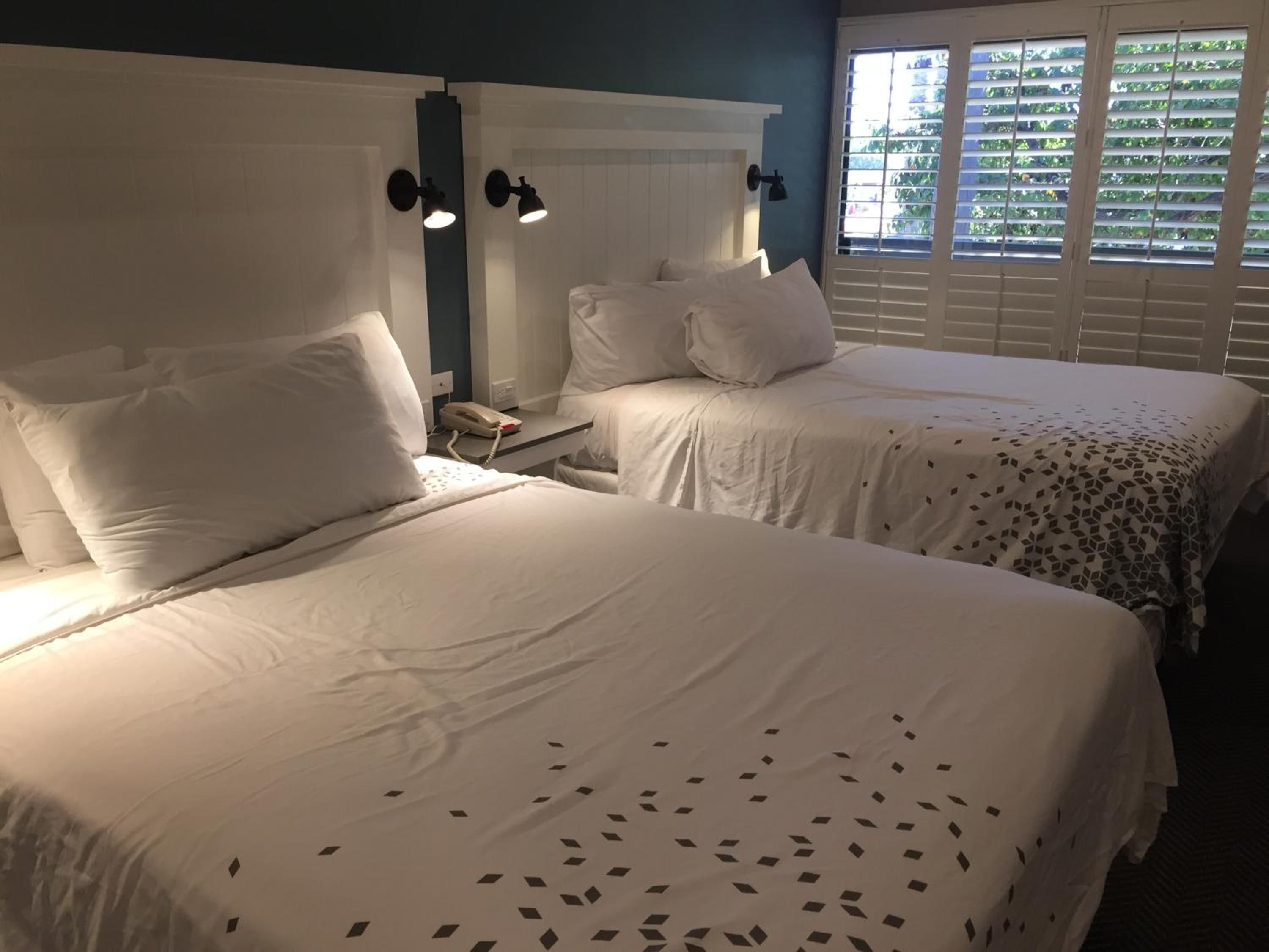 A hotel room with two beds, white bedding, a telephone on the nightstand, and wall-mounted lamps.