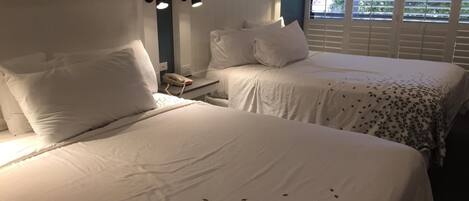 A hotel room with two beds, white bedding, a telephone on the nightstand, and wall-mounted lamps.