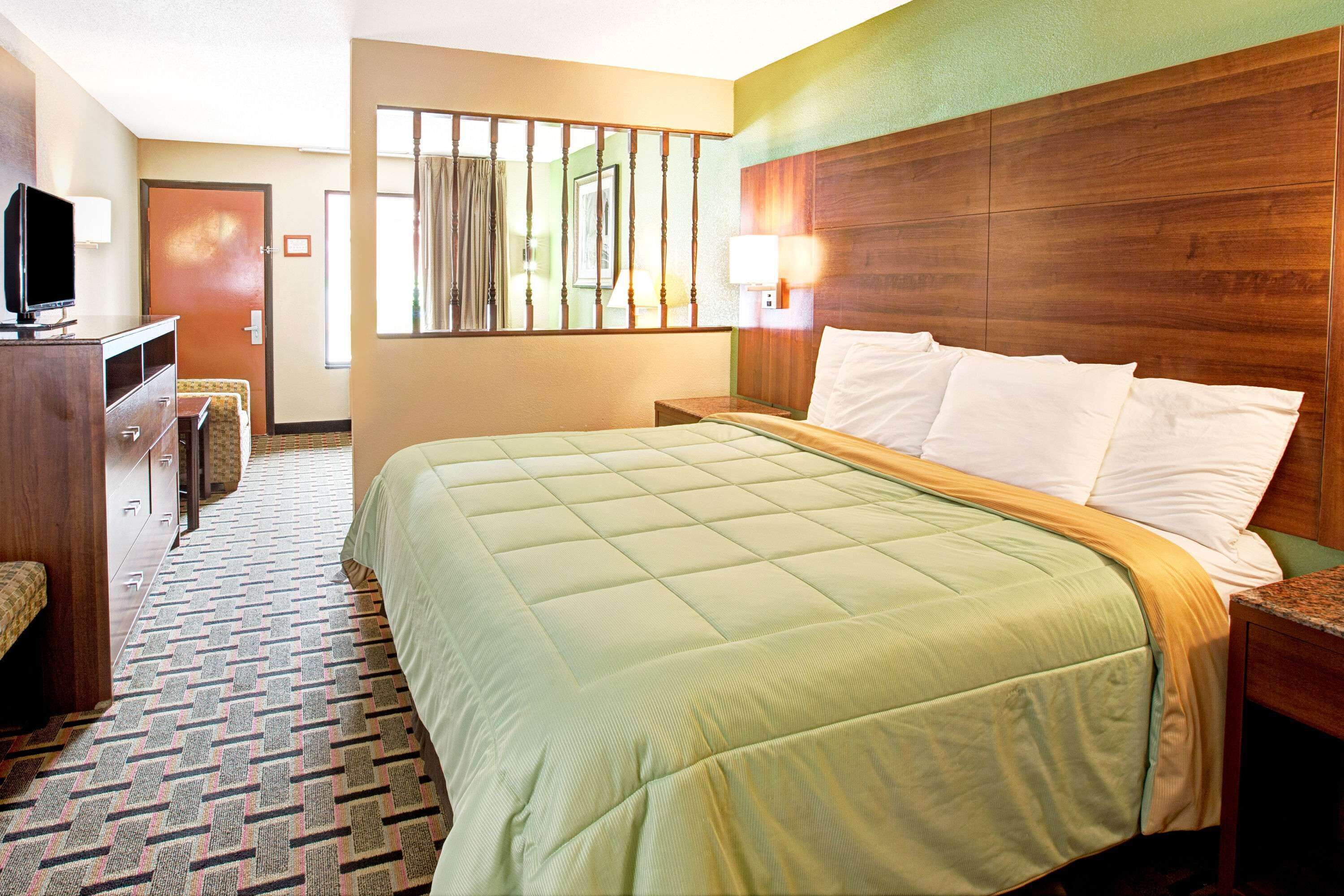 Habitación de hotel con una cama grande, un escritorio con televisor, una silla y una ventana con cortinas.