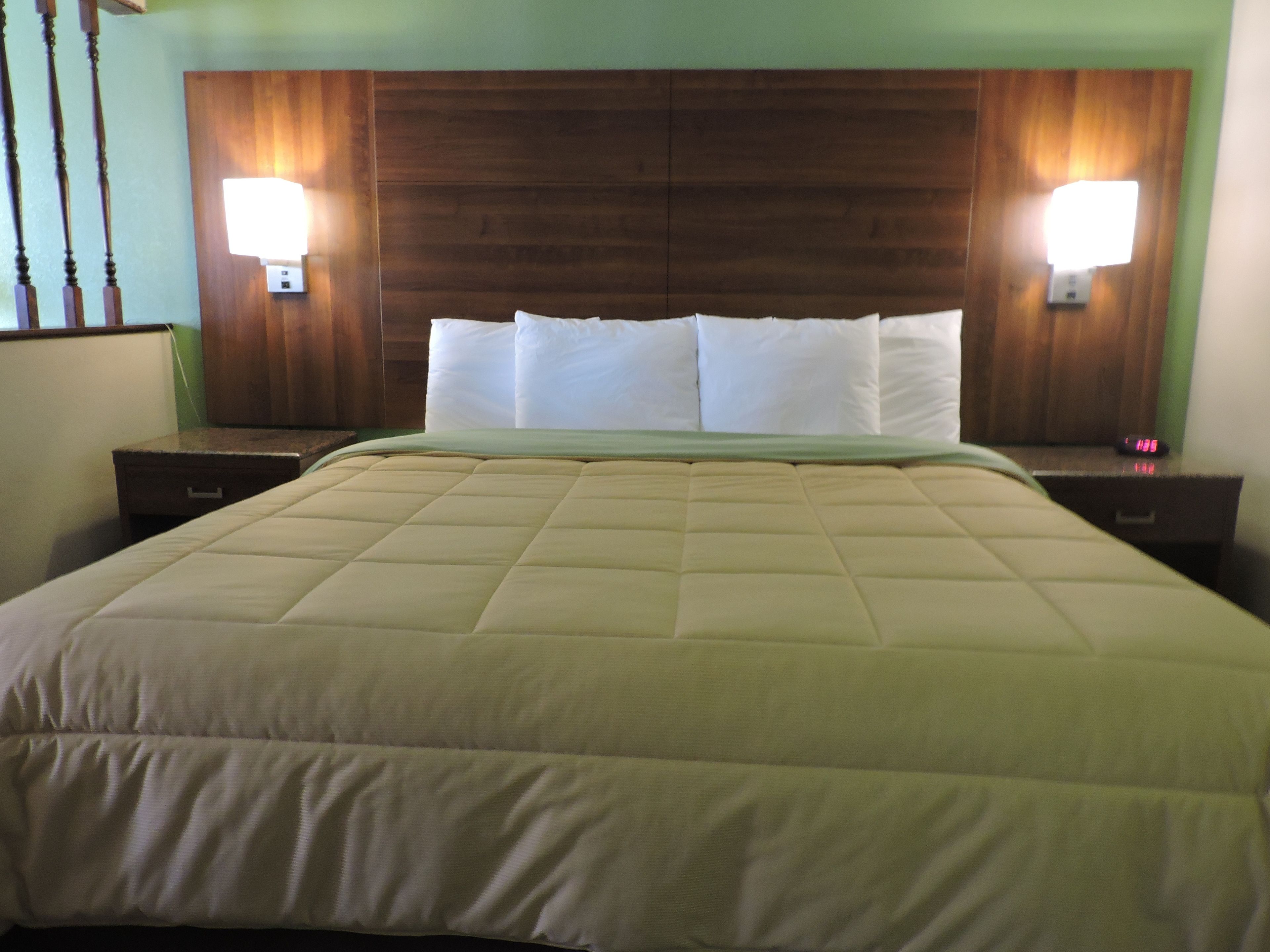 Een hotelkamer met een groot bed, een houten hoofdeinde, twee nachtkastjes met lampen, en een groene muur.