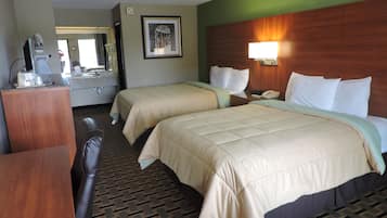 A hotel room with two beds, a desk, a mirror, and a bathroom visible through an open door.