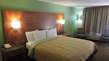A hotel room with a large bed, two bedside lamps, a nightstand with a phone, a chair, and a window with curtains.