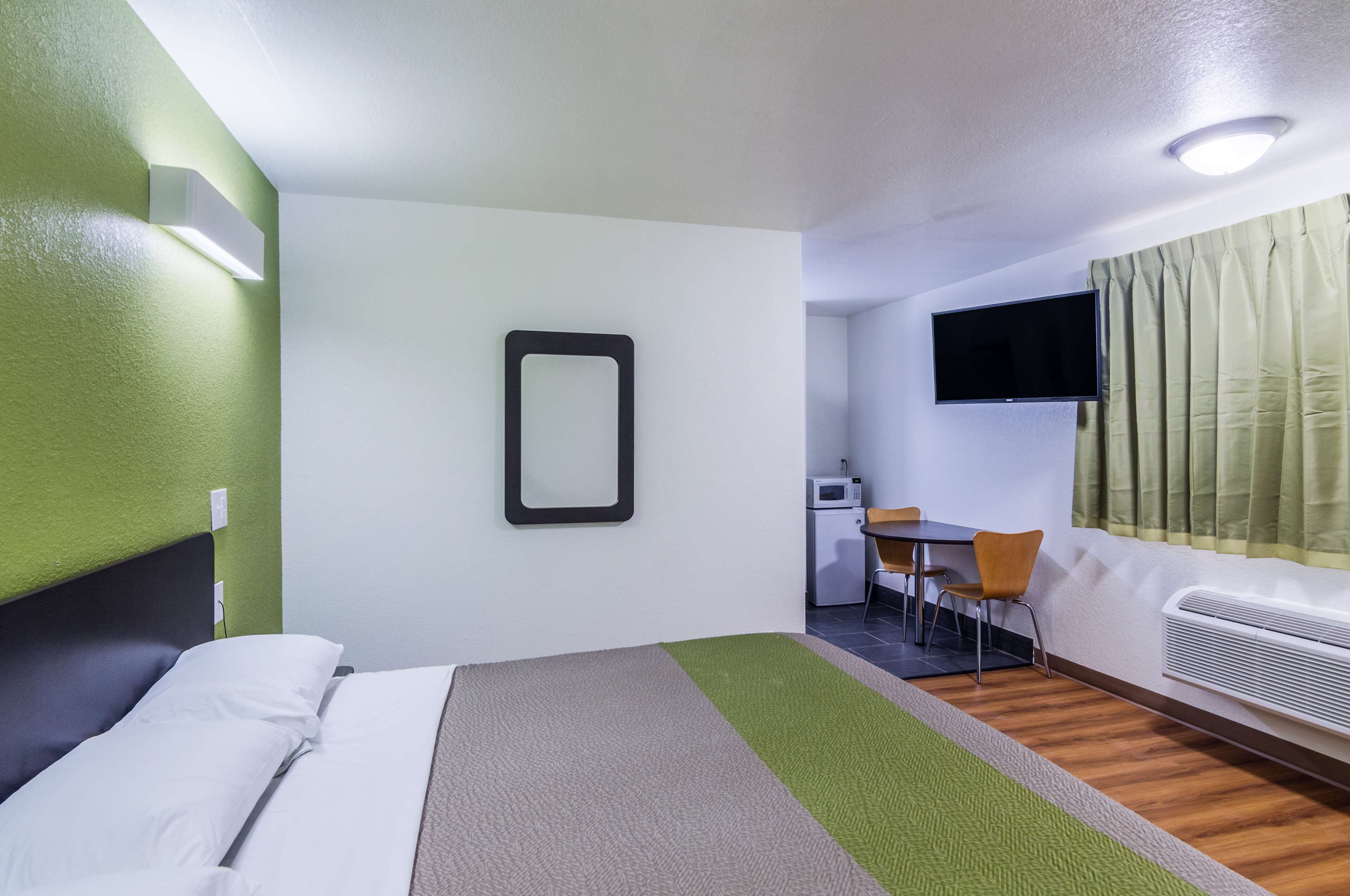 A hotel room with a bed, a desk with a chair, a television, and a window with curtains.