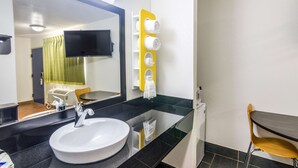 Un baño moderno con un espejo grande, un lavamanos, un perchero para toallas y una pequeña mesa con una silla.