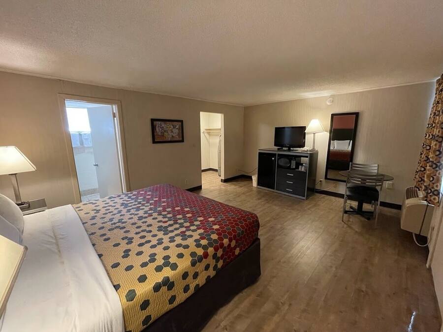 A hotel room with a large bed, a desk with a chair, a television, and a bathroom visible through an open door.