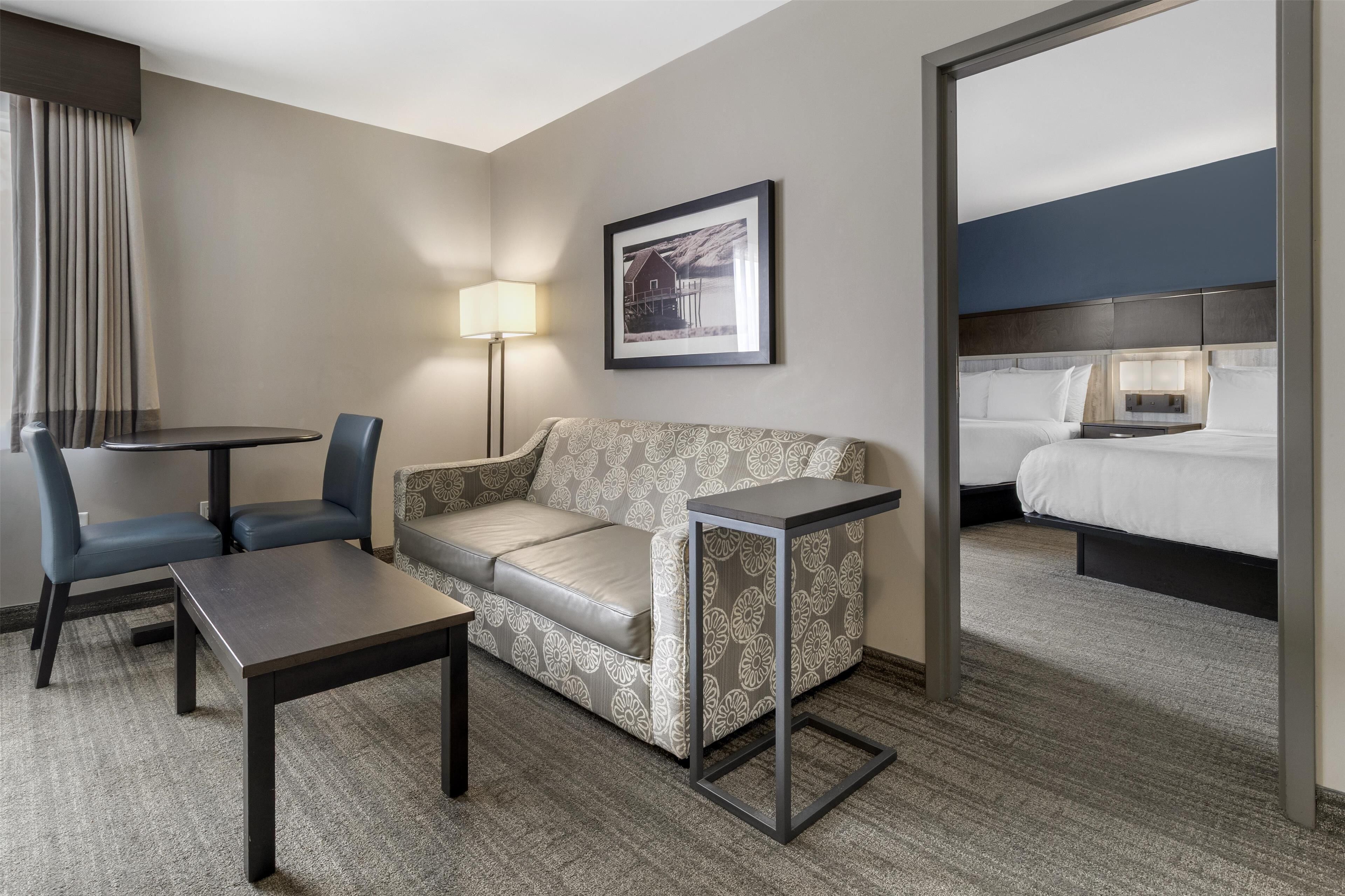 Quarto de hotel com sofá, mesa pequena, luminária e cama.