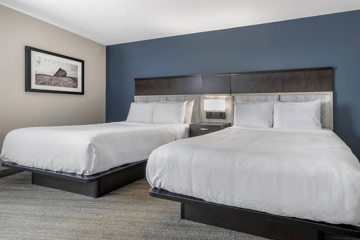 A hotel room with two beds, a framed picture on the wall, and a dark headboard.