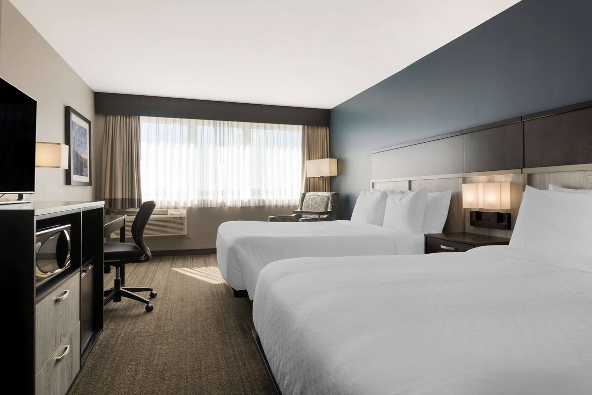 A hotel room with two beds, a desk with a chair, a TV, and a window with curtains.