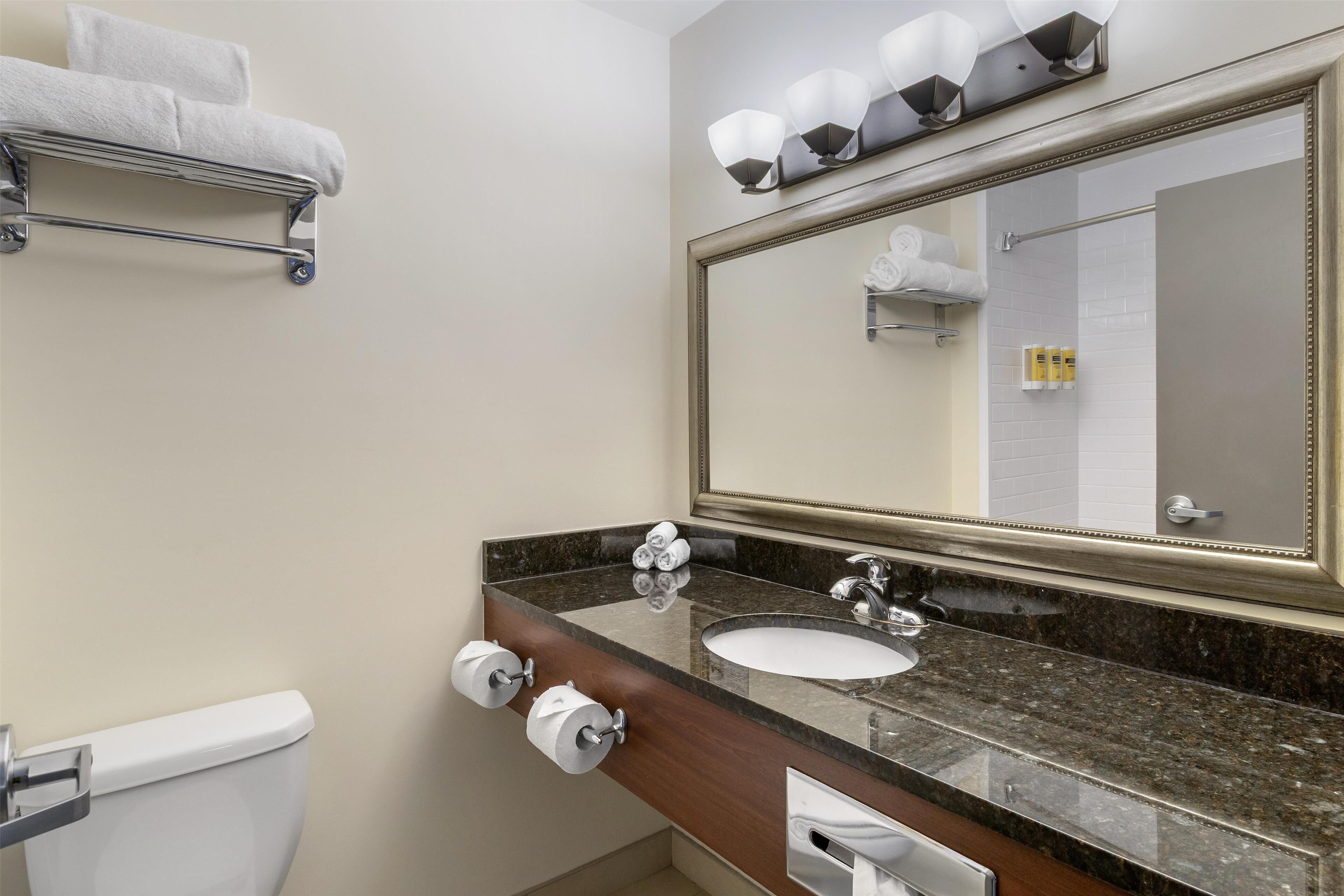 Un baño con lavamanos, espejo, toallero y retrete.