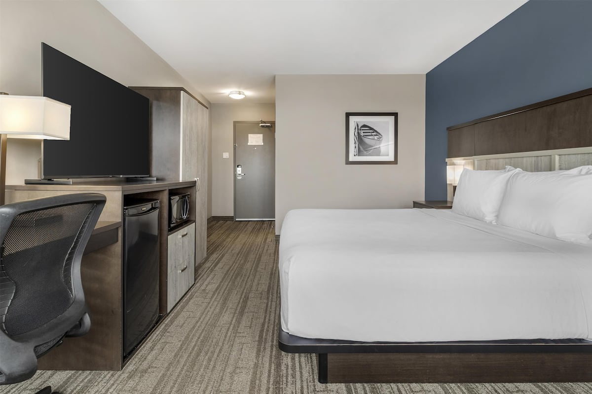 A hotel room with a bed, desk, chair, TV, and a framed picture on the wall.