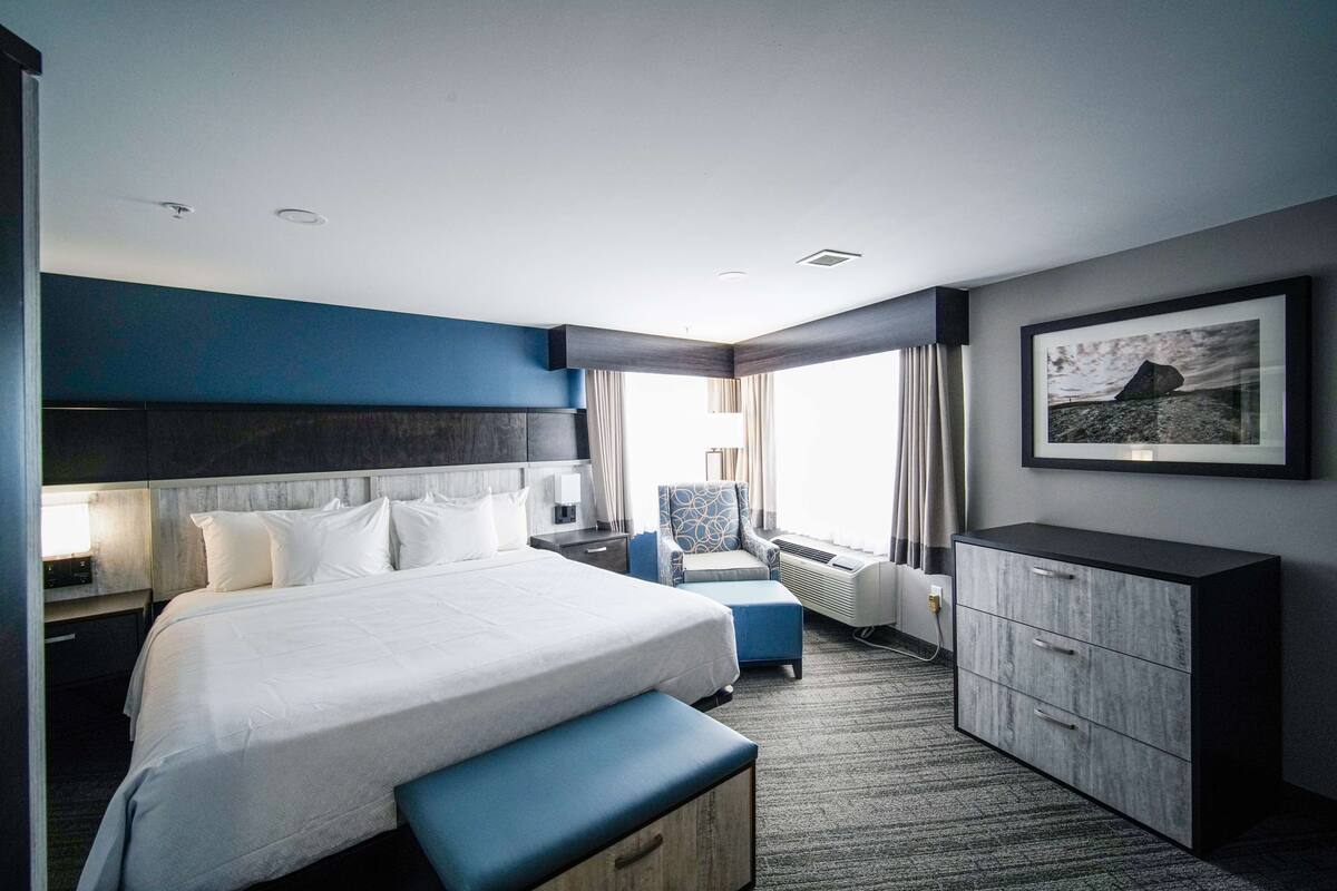 A modern hotel room with a large bed, a desk, a chair, and a wardrobe.