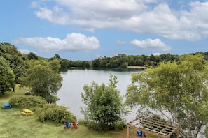 A lakeside camping area with picnic tables, a wooden pergola, and a small house in the background.