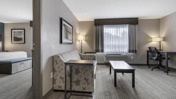 A hotel room with a bed, a sofa, a small table, a desk, and a chair. There are two lamps and a window with curtains.