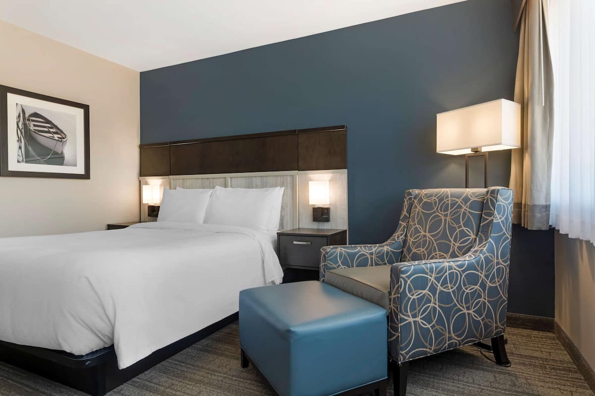 A hotel room with a bed, a nightstand, a chair, and a lamp.