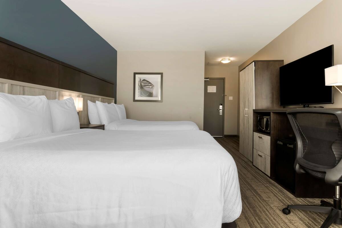 A hotel room with two beds, a desk, a television, and a microwave.