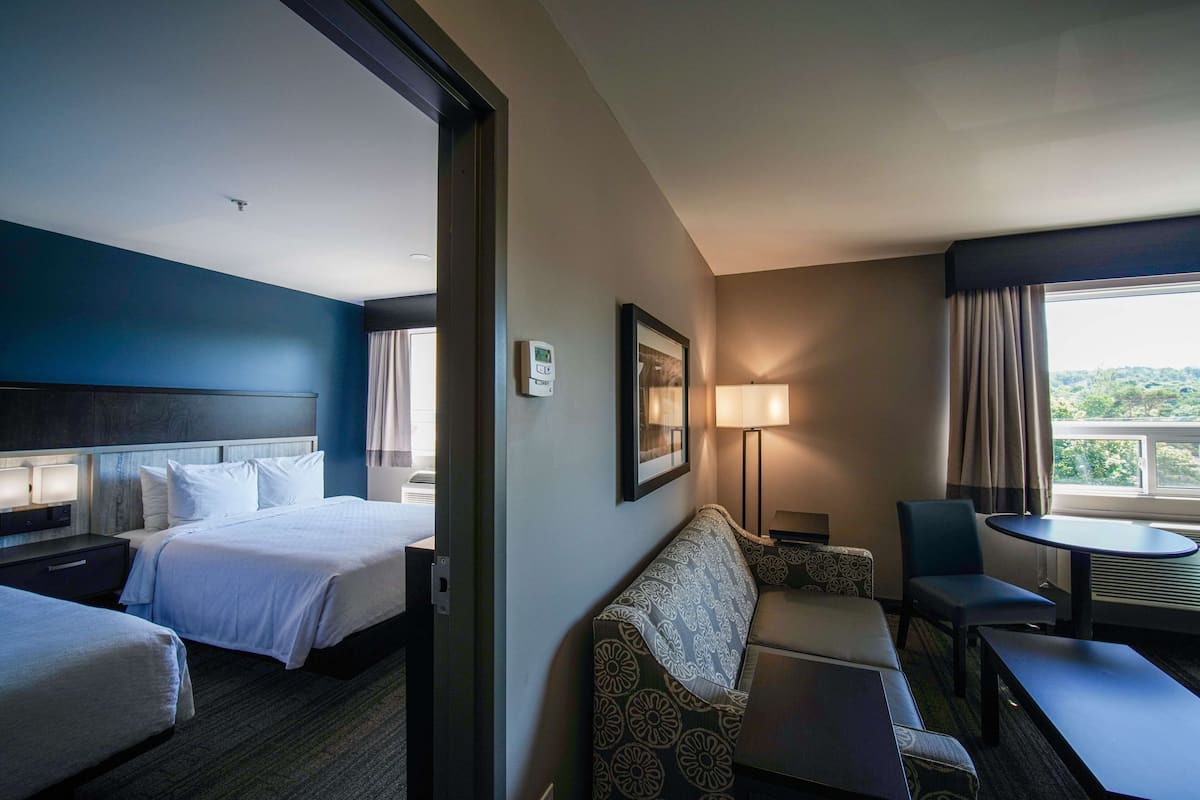 A hotel room with two beds, a sofa, a table, and a view of the outdoors.