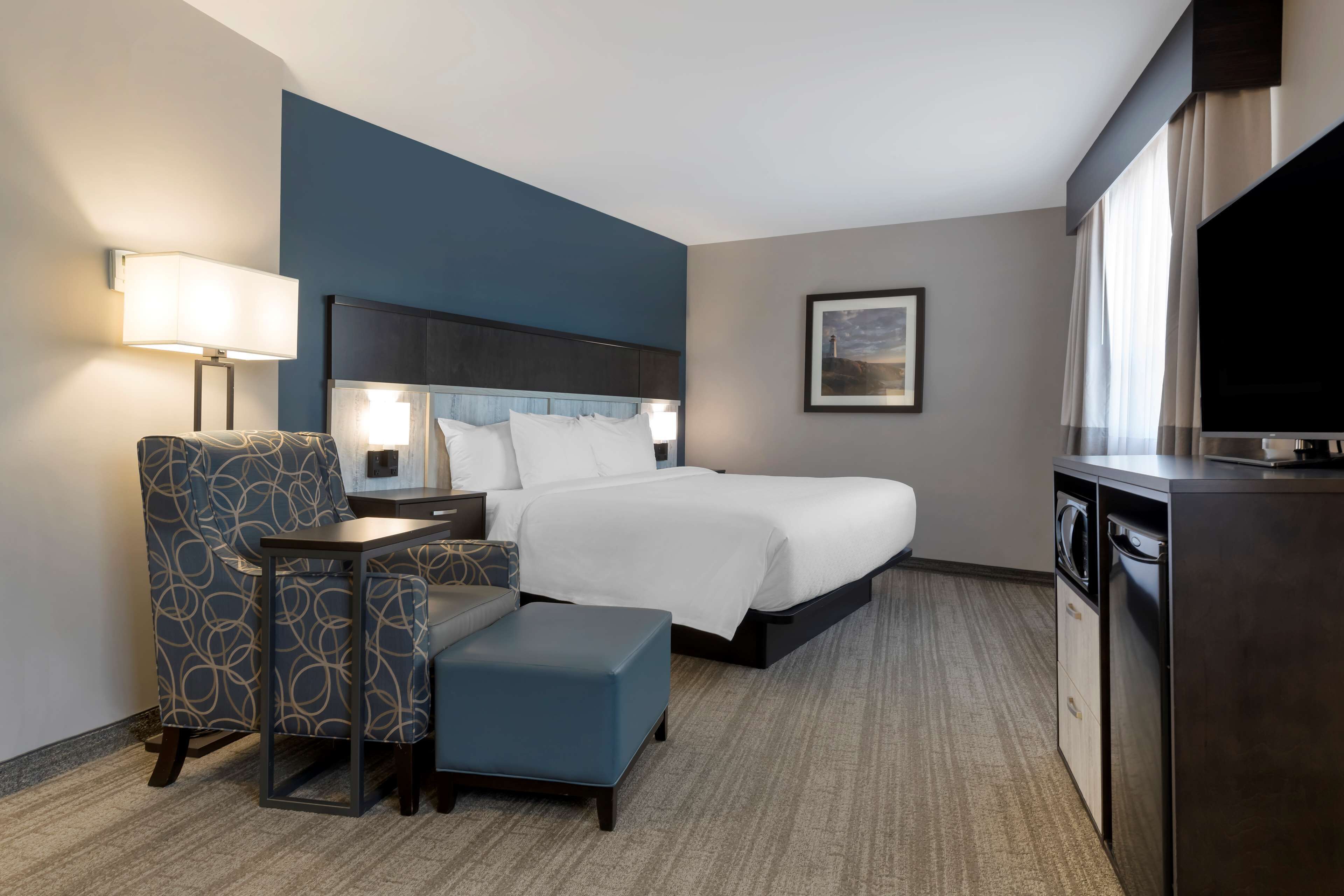 A hotel room with a bed, a desk with a chair, a television, and a washing machine.