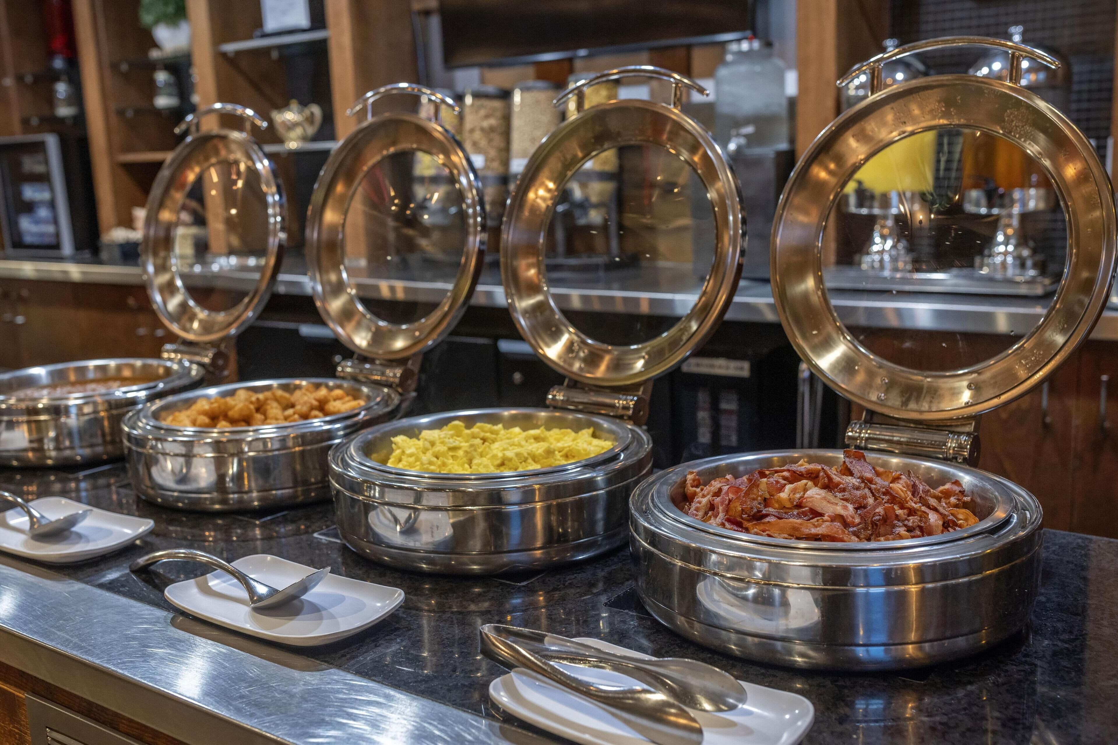 A buffet with various food items in stainless steel bowls, each with a lid.
