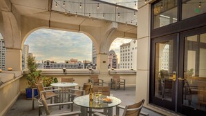 A rooftop terrace with round tables and chairs, potted plants, and a view of the city skyline. - The Donatello (San Francisco)