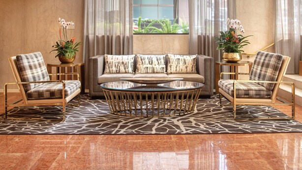 A spacious lobby with a large chandelier, a sofa set, two armchairs, a glass-top coffee table, and a view through a large window. - The Donatello (San Francisco)