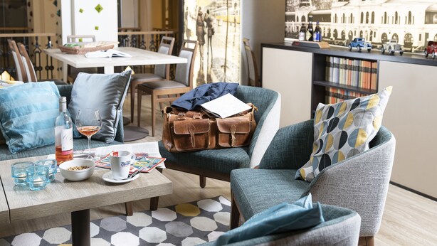 A cozy seating area with a table set for two, a bookshelf, and a view of a historic building. - Three Corners Hotel Art (Budapest)