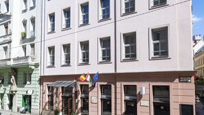 A multi-story building with a prominent clock tower, large windows, and a flag display. - Three Corners Hotel Art (Budapest)
