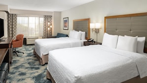 A hotel room with two beds, a desk with a chair, a TV, and a window with curtains.