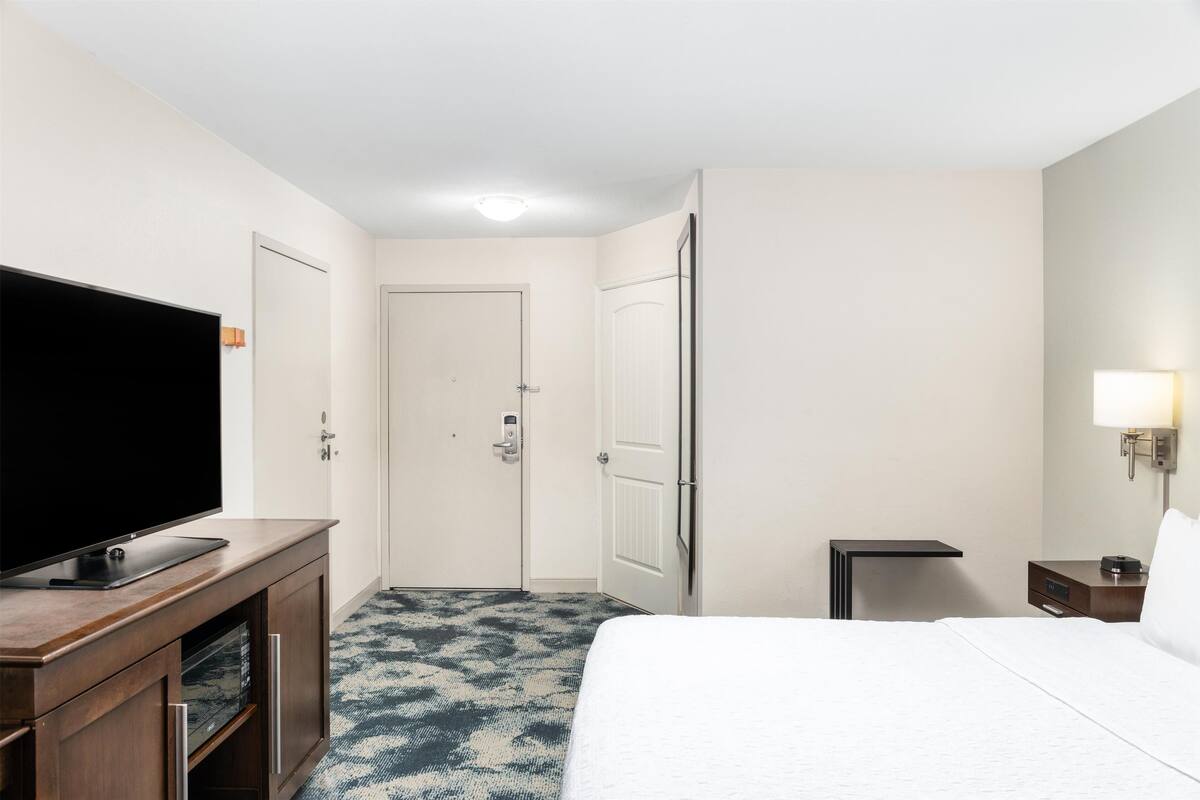 A hotel room with a bed, a TV on a wooden console, a door, a nightstand, and a lamp.